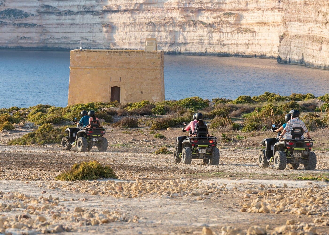Quad bikes on a Gozo coastal track toward Xlendi Tower and the cliffs.